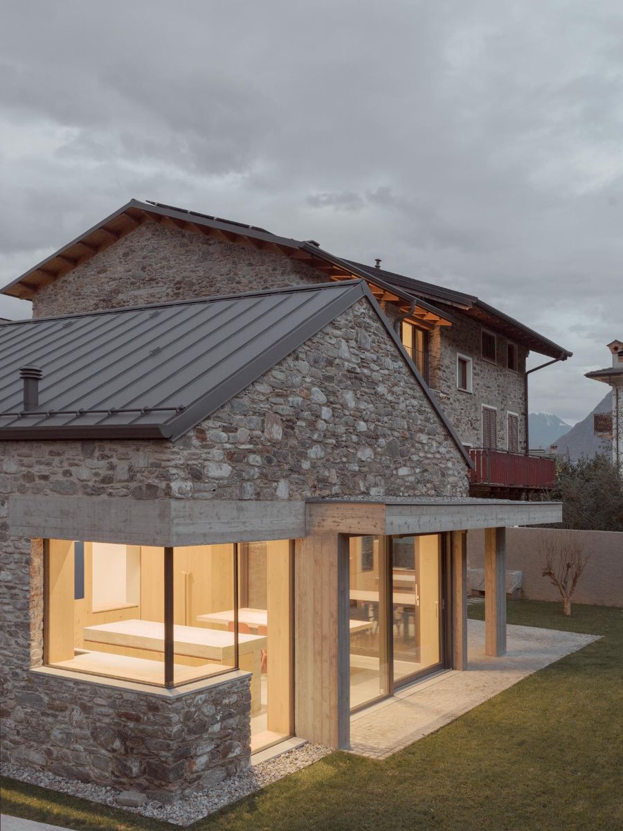 Exteriér kamenného domu s plechovou strechou a presvetlenou prístavbou s veľkými oknami.