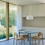 Modrý okrúhly jedálenský stôl s drevenými stoličkami pri bielych minimalistických kuchynských skrinkách.