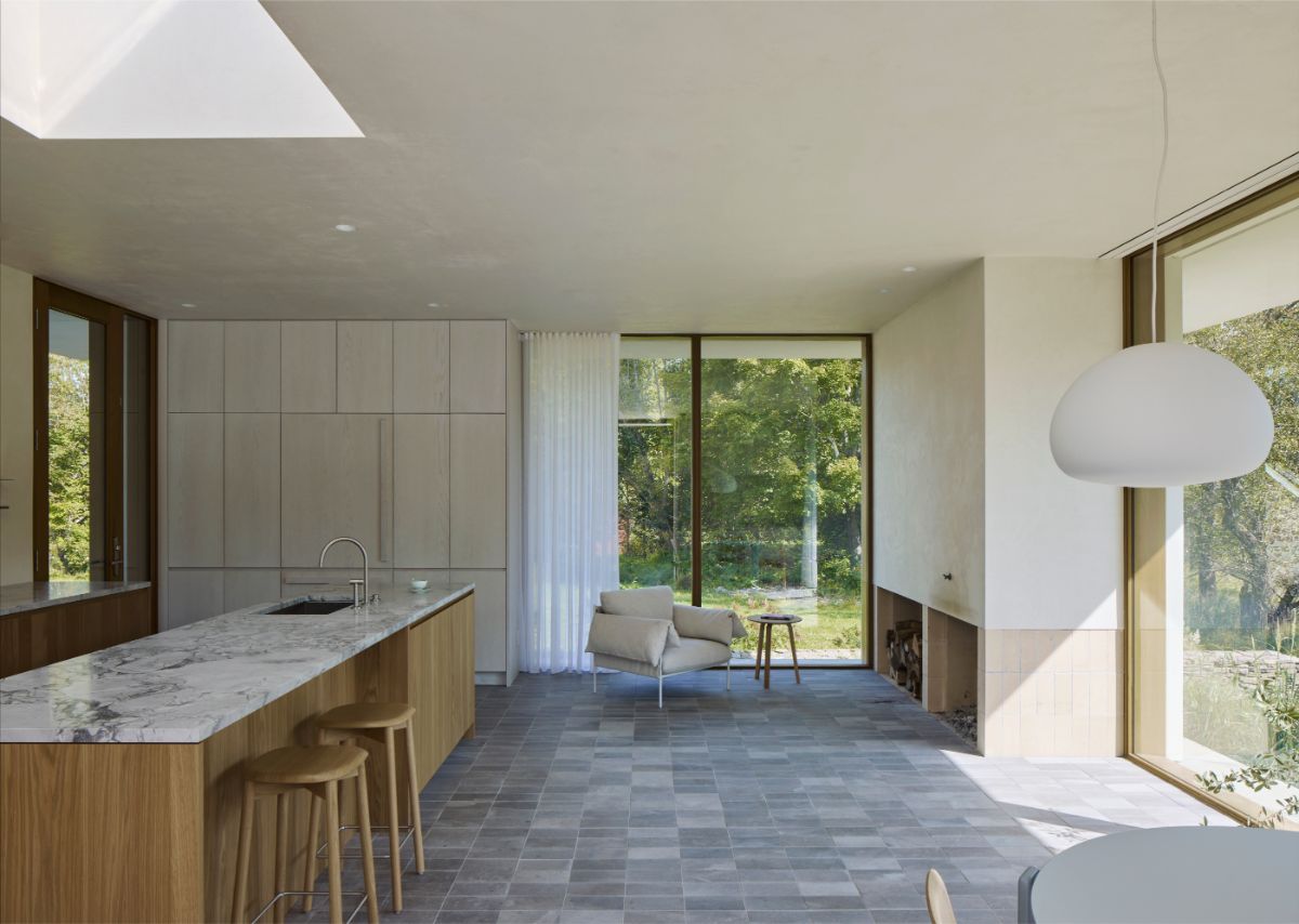 Kuchynský ostrov s mramorovanou doskou, drevené barové stoličky a svetlé kreslo v otvorenom interiéri.