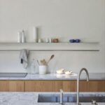 Kuchynská linka s mramorovou pracovnou doskou, zapusteným drezom a drevenými skrinkami pod otvorenou policou.