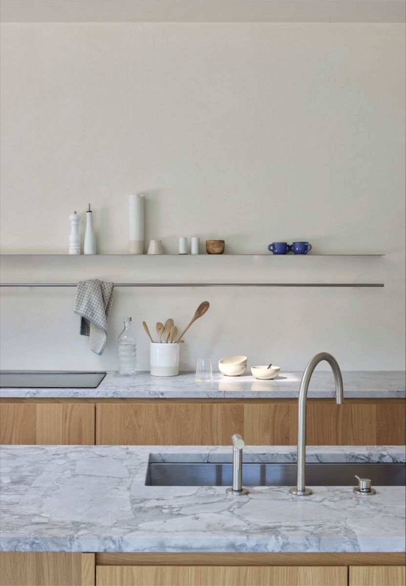 Kuchynská linka s mramorovou pracovnou doskou, zapusteným drezom a drevenými skrinkami pod otvorenou policou.