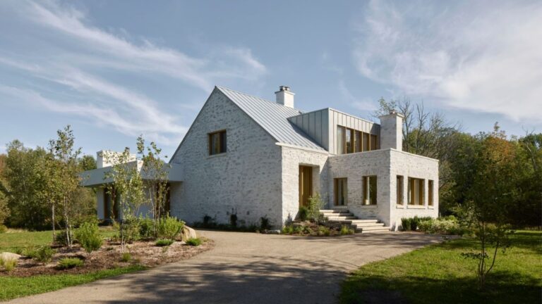 Biely kamenný dom s modernou prístavbou, výrazným komínom a príjazdovou cestou.