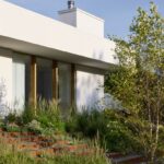 Fasáda s veľkoformátovým oknom, ku ktorým vedie exteriérové schodisko so záhonom.