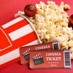 Popcorn a lístky do kina na červenom pozadí.