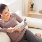 Žena pri čítaní knihy na sedačke.