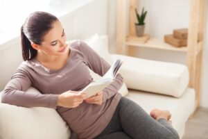 Žena pri čítaní knihy na sedačke.