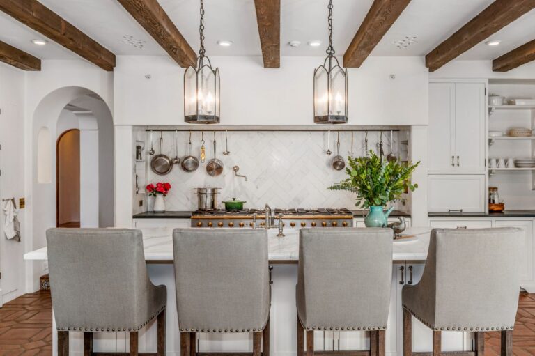 Kuchyňa v modernom farmárskom štýle s bielou linkou, ostrovčekom a stoličkami, viditeľnými trámami a osvetlením v štýle lampášov.