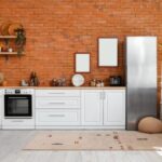 Moderná biela kuchyňa so spotrebičmi a tehlovou stenou.