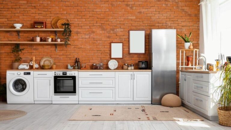 Moderná biela kuchyňa so spotrebičmi a tehlovou stenou.