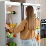 Mladá žena stojí pri otvorenej chladničke.