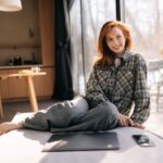 Žena v károvanej košeli sediaca na svetlom matraci v modernom presvetlenom byte.