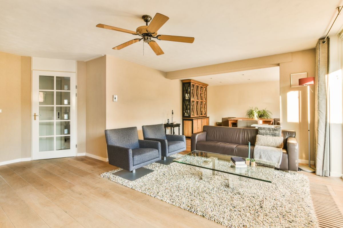 Moderná obývacia izba s béžovými stenami, dreveným stropným ventilátorom a hnedou koženou sedačkou.