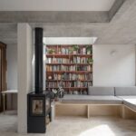 Moderná minimalistická sedačka pri kachľovej peci a terakotovej knižnici v pozadí.