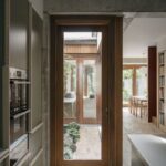 Drevené presklené dvere výhľadom do átria so zeleňou vedúce z moderne zariadenej kuchyne.