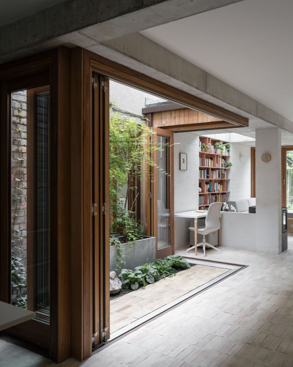 Harmonikové dvere otvorené do átria s betónovým kvetináčom a tehlovou dlažbou.