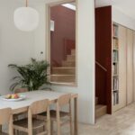 Drevený stôl pri schodisku s červenou stenou, viditeľnou cez sklenenú stenu.