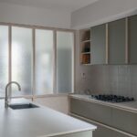 Kuchynský ostrov pred stenou z mliečneho skla a zelenou linkou s vertikálnym obkladom.