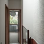 Chodba so skleneným zábradlím pod svetlíkom vedľa bielej tehlovej steny.