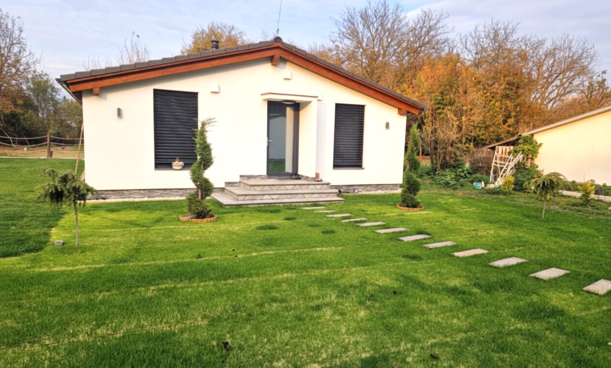 Rodinný bungalov so sedlovou strechou a dláždeným chodníkom v tráve.