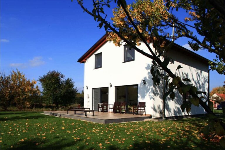 Moderný poschodový rodinný dom so sedlovou strechou a a bielou omietkou.