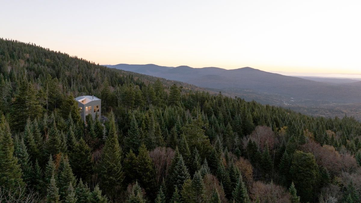 Pohľad z diaľky na poschodový dom v ihličnatom lese.