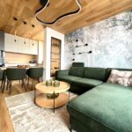 Obývacia izba so zelenou sedačkou, dizajnovou tapetou s motívom lesa a dreveným stropným obkladom.