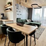 Jedálenský kút s masívnou dubovou doskou, tmavozelenými stoličkami a výhľadom na obývaciu časť s balkónom.