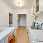 Staršia kuchynská linka s bielymi profilovanými dvierkami, antikorovým drezom a svetlým jedálenským stolom.