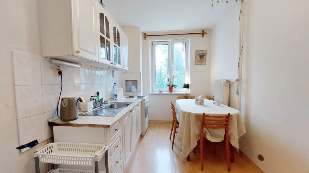 Biela retro kuchyňa s antikorovým drezom a jedálenským stolom s obrusom.