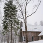 Časť domu s komínom so sedlovou strechou a drevenou fasádou v zime.