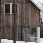 Časť rodinného domu s drevenou fasádou a presklením v zimnom lese.