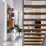 Pohľad do obývacej izby s nadčasovým zeleným kreslom cez drevené stupne schodiska.