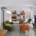 Presvetlená obývacia izba s čiernym krbom, zelenou pohovkou, koženými kreslami a minimalistickými nástennými policami.