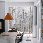 Jedálenský kút s dreveným stolom a stoličkou pri veľkoformátovom okne s výhľadom na zasnežený les.