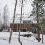 Rodinný dom so sedlovou strechou, drevenou fasádou a veľkoformátovými oknami v zime v lese.