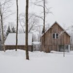 Drevené domy prepojené strieškou s drevenou fasádou a sedlovou strechou v zasneženom lese.