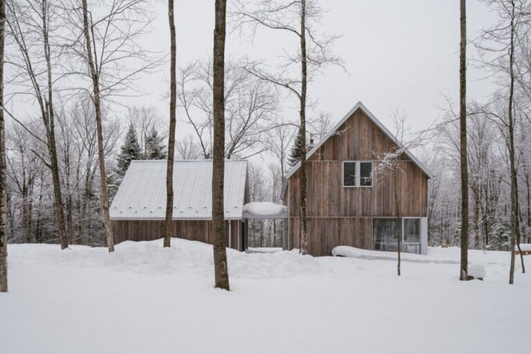 Drevené domy prepojené strieškou s drevenou fasádou a sedlovou strechou v zasneženom lese.