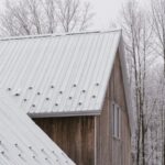 Zasnežená sedlová strecha rodinného domu s drevenou fasádou v lese.