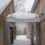 Zasnežená strieška, spájajúca dva domu s drevenou fasádou.