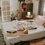 Neupravená posteľ v spálni s krabicou od pizze, zvyškami jedla a rozhádzaným oblečením.