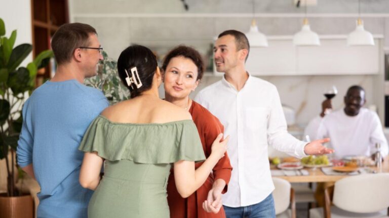 Skupina priateľov v modernej kuchyni počas srdečného vítania hostí pri prestretom jedálenskom stole.