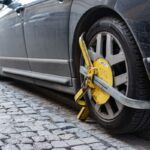 Čierne auto na kamennej dlažbe s nasadenou papučou na prednom kolese.