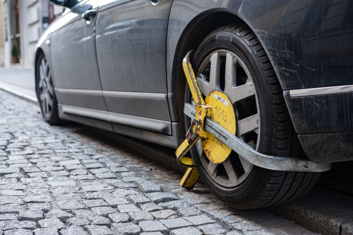 Čierne auto na kamennej dlažbe s nasadenou papučou na prednom kolese.