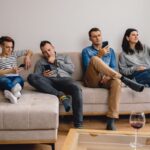 Štyria dospelí ľudia sediaci na svetlej pohovke a mobilmi ruke počas návštevy.