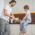 Mladý muž v pyžame zalieva mliekom müsli pre malého chlapca.