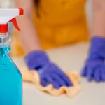 Čistiaci prostriedok na pracovnej doske kuchynskej linky, v pozadí žena upratuje.