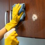 Striekanie čistiaceho prostriedku na drevenú kuchynskú skrinku.