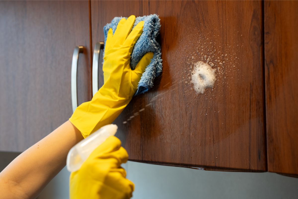Striekanie čistiaceho prostriedku na drevenú kuchynskú skrinku.