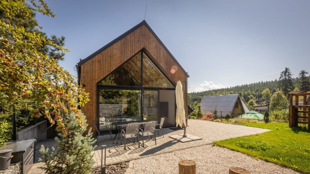 Moderná drevená chata so šikmou strechou a veľkým preskleným štítom, s terasou s posedením a štrkovou záhradou.