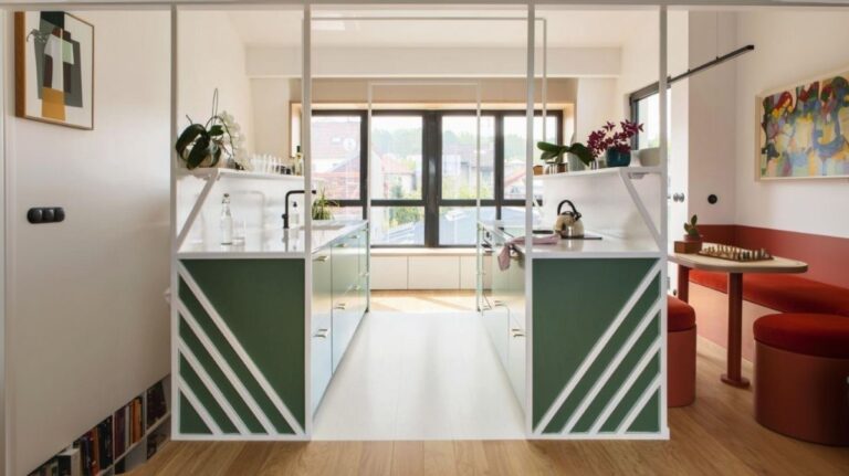 Symetrická kuchynská linka so zelenými skrinkami, bielou pracovnou doskou a bielym oceľovým rámom v loftovom interiéri.